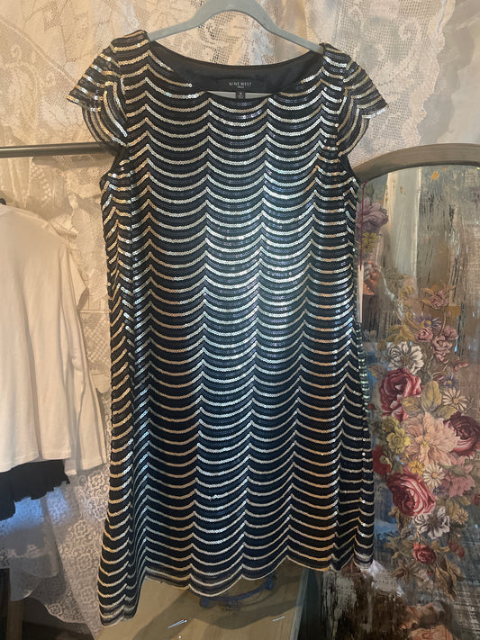 A sleeveless A-line dress with a wavy, scalloped pattern of black and gold sequins, hanging on a hanger.
