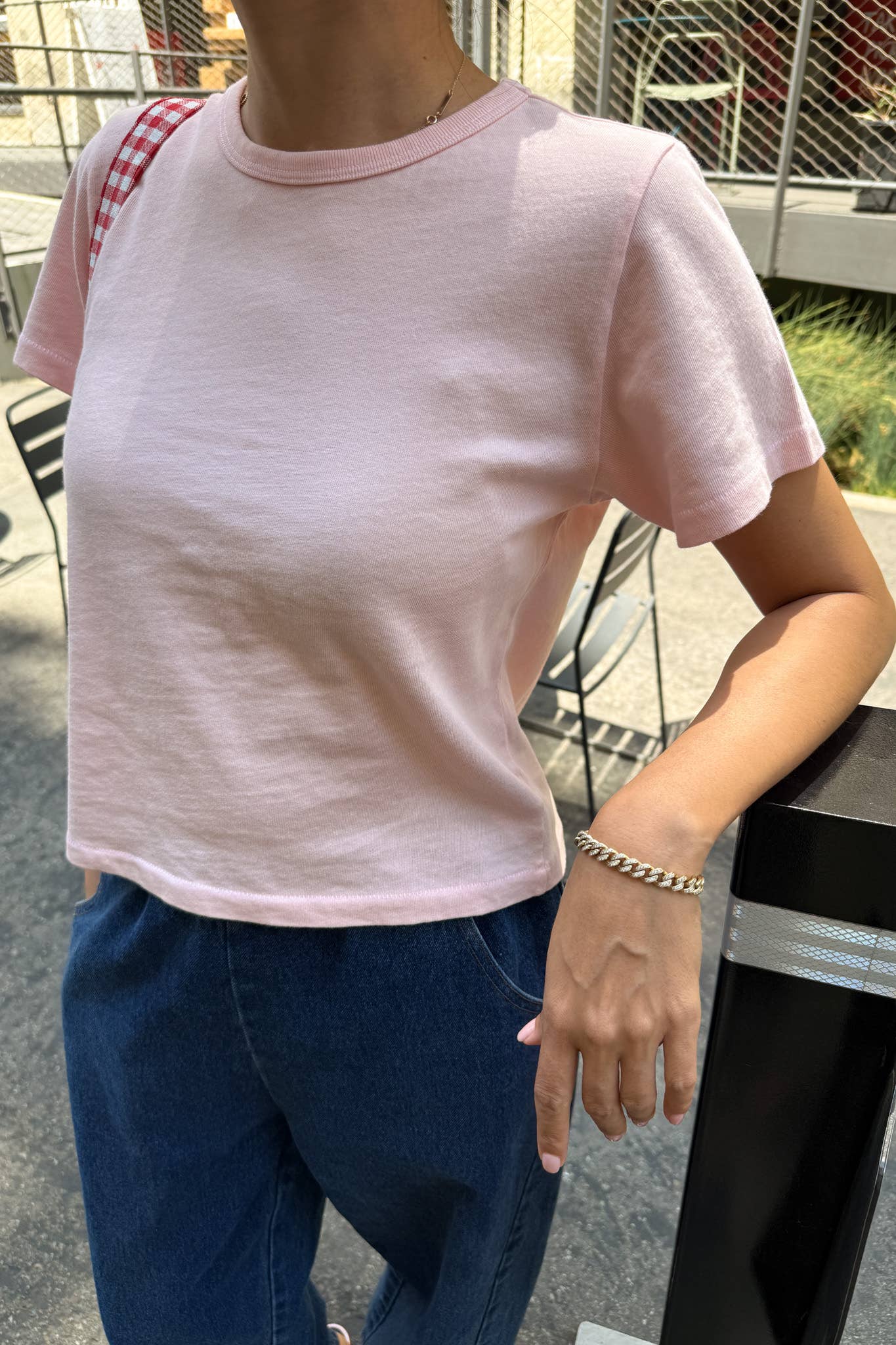 Person wearing a pink t-shirt and blue jeans standing outdoors.